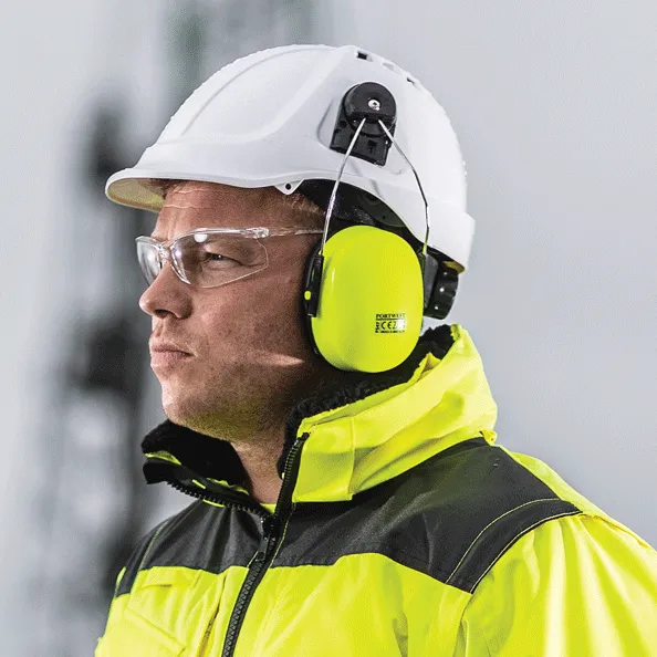 Seorang pekerja mengenakan alat pelindung diri lengkap: helm safety putih, kacamata pelindung, dan earmuff Portwest untuk perlindungan kepala, mata, dan pendengaran.